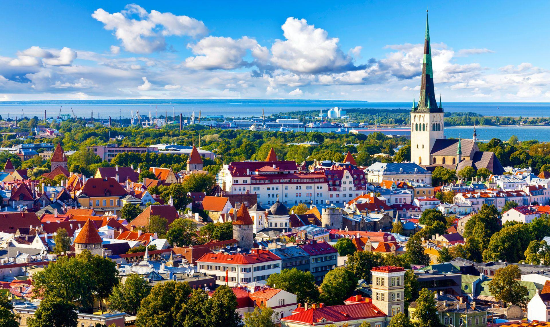 Panoramic view of Tallinn Old Town in Estonia featuring the historic St. Olaf's Church spire and red roofed medieval architecture against the Baltic Sea.